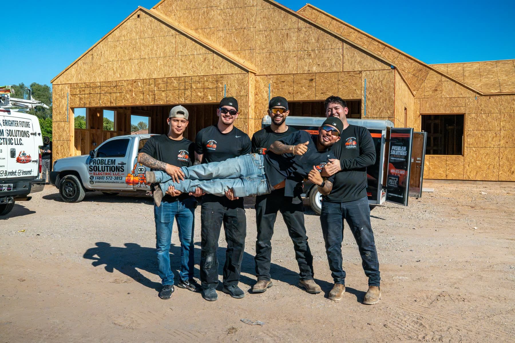 The crew joking around in front of a framed home, with both company trucks and the trailer behind them