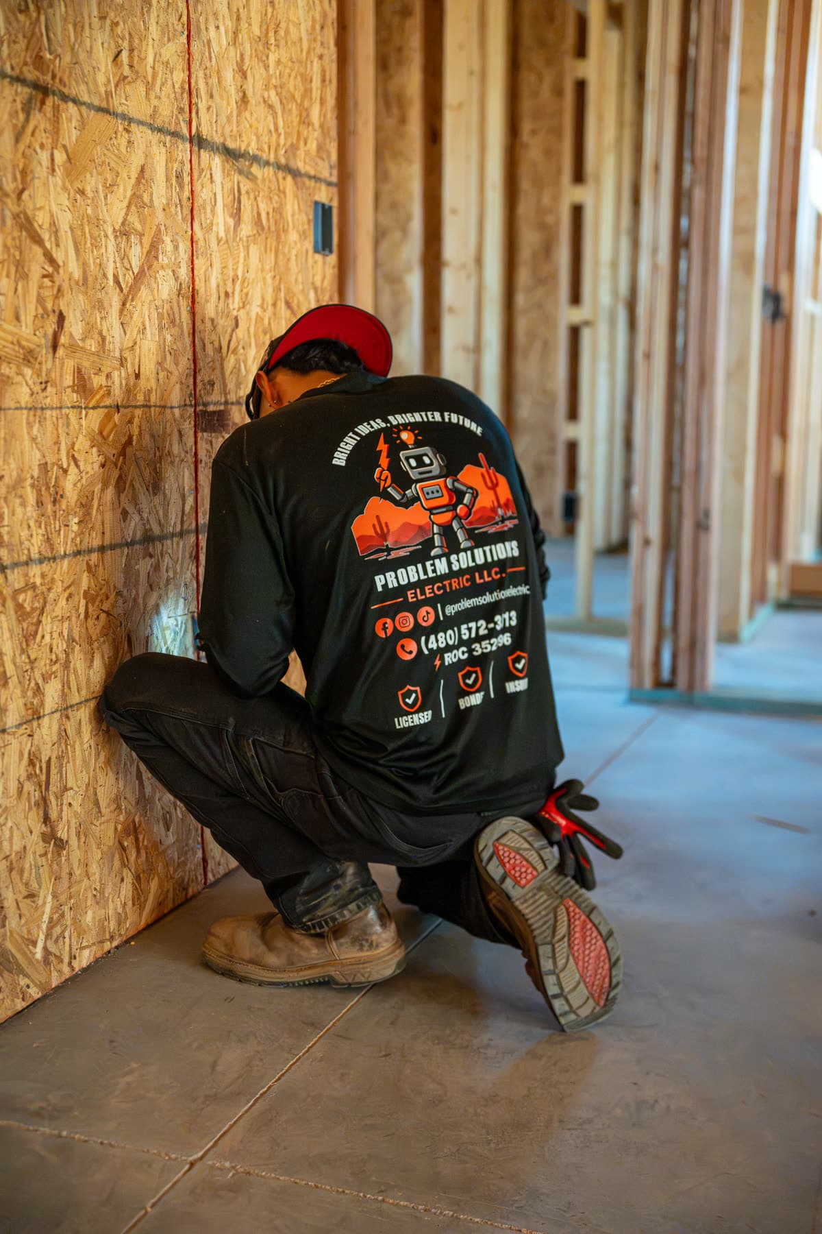 A technician kneeling at a framed wall, the robot logo on his shirt
